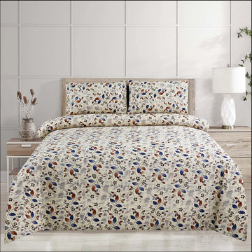 Floral patterned bedding set on a bed with matching pillows and a lamp in the background.