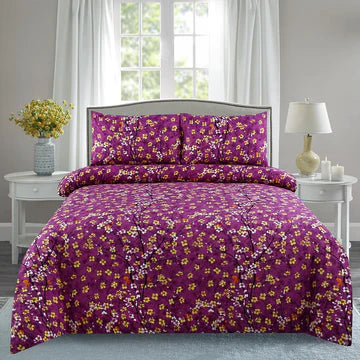 Purple floral comforter set on a bed in a bedroom with white curtains and a lamp.