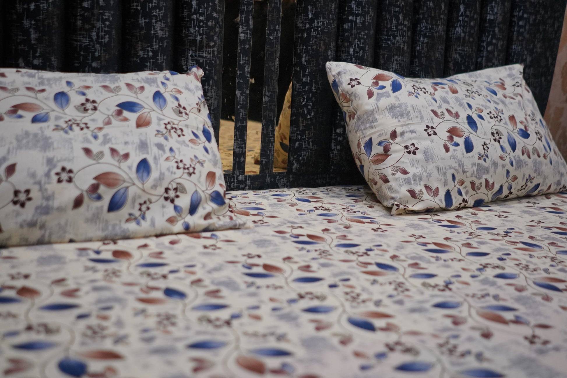 Floral-patterned bedspread and pillows on a bed with a dark headboard.