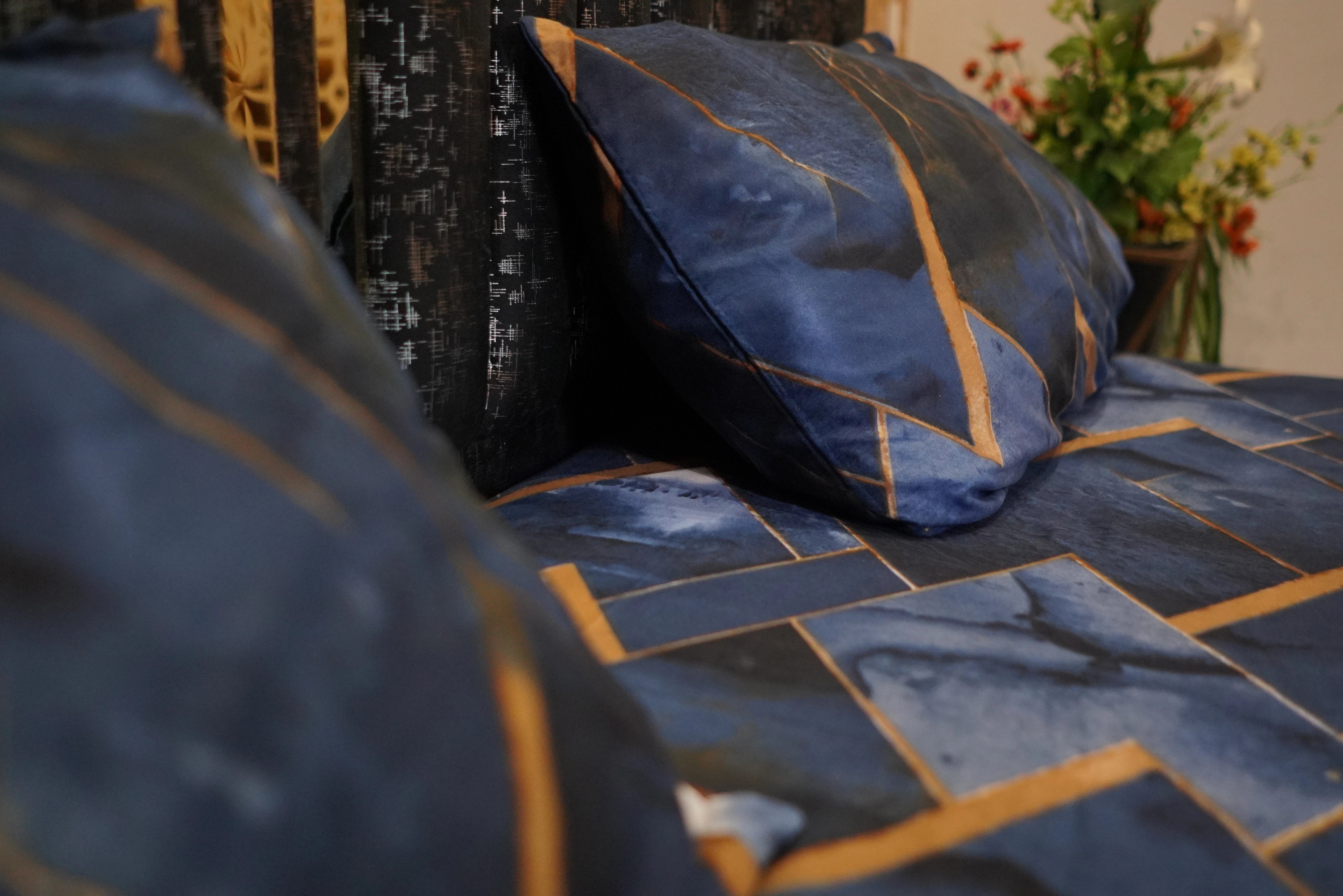 Blue quilt with gold accents on a bed, with a pillow in the foreground.