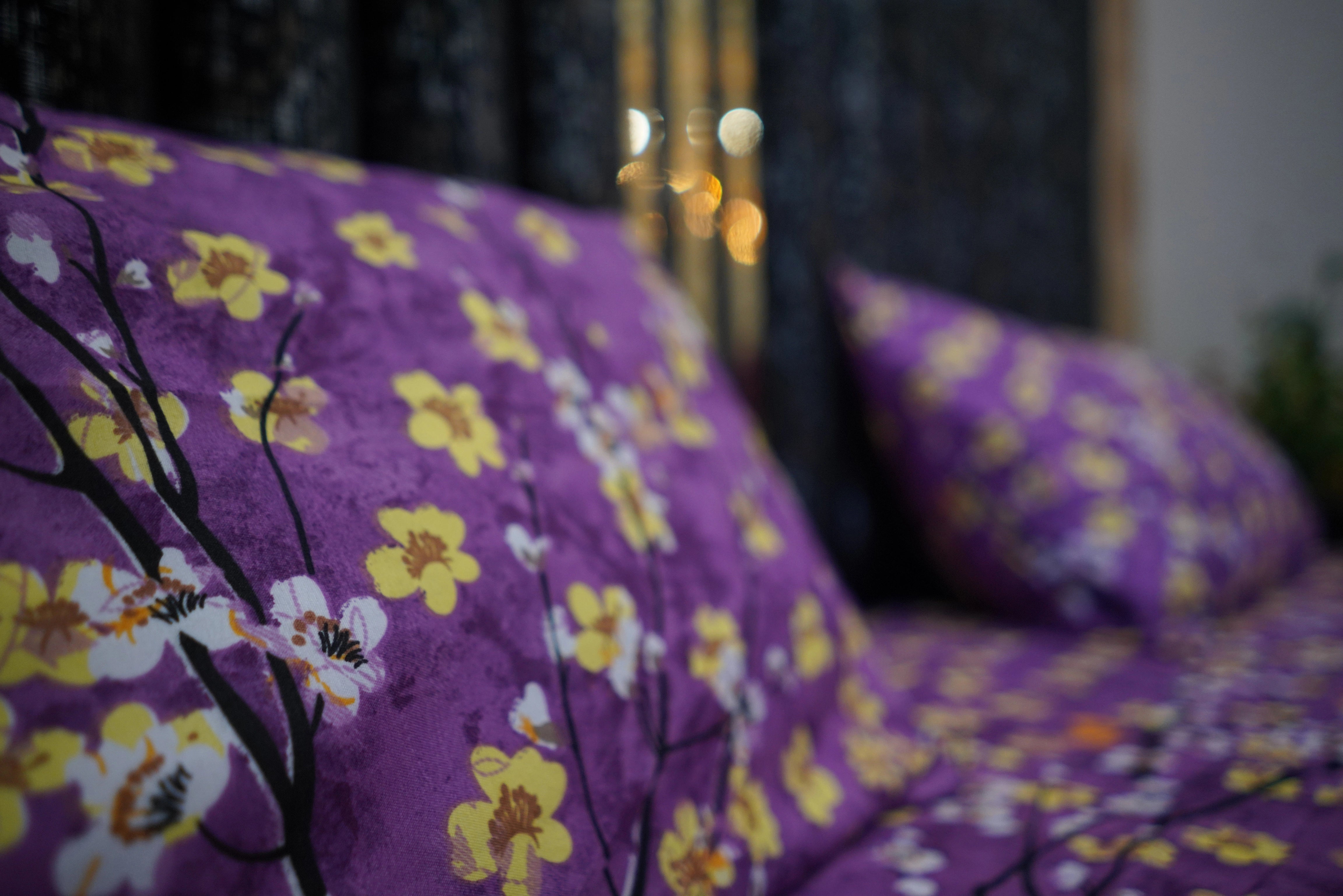 Purple floral patterned fabric with yellow flowers on a bed.