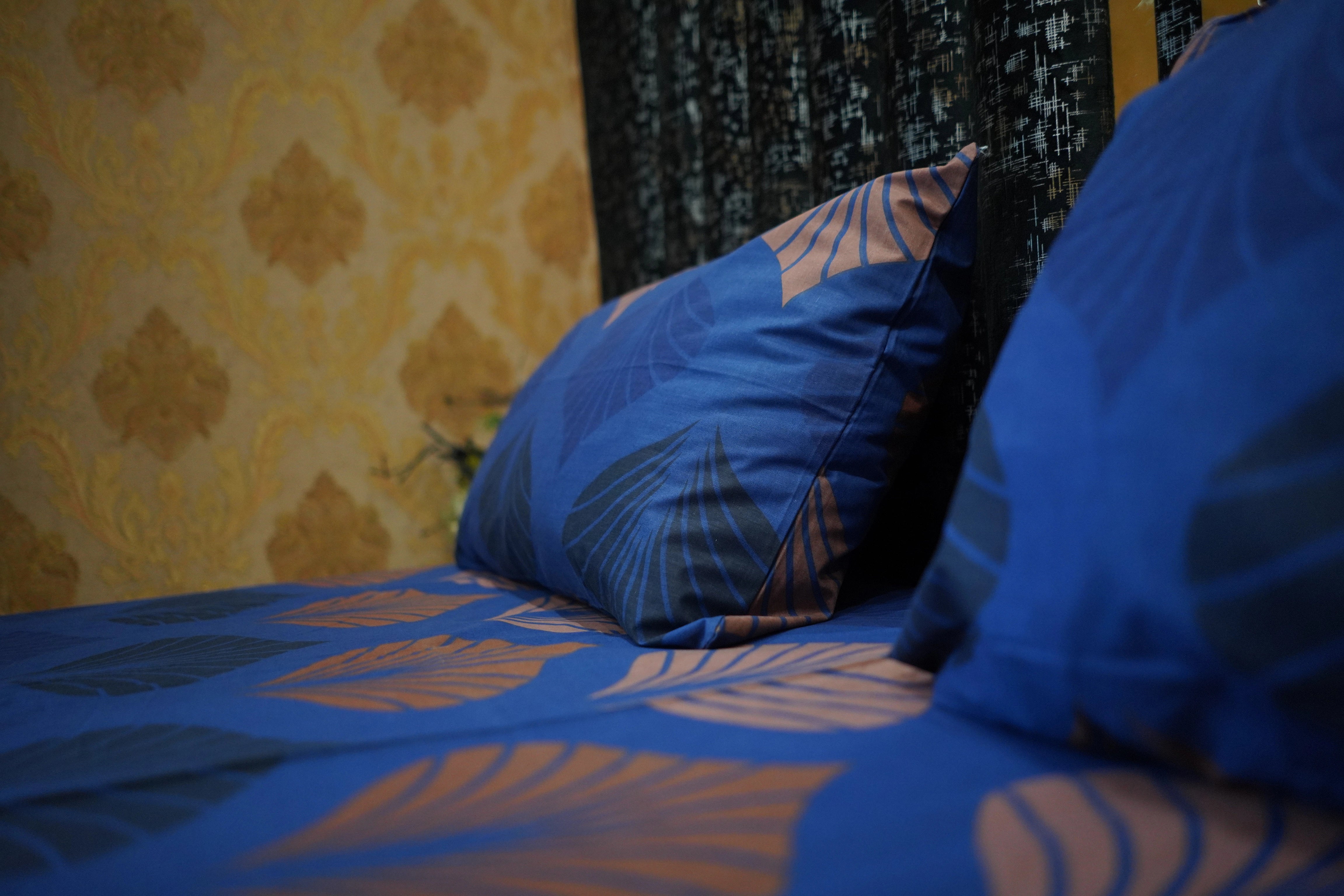 Blue patterned pillows on a bed with yellow and black textured wall in the background