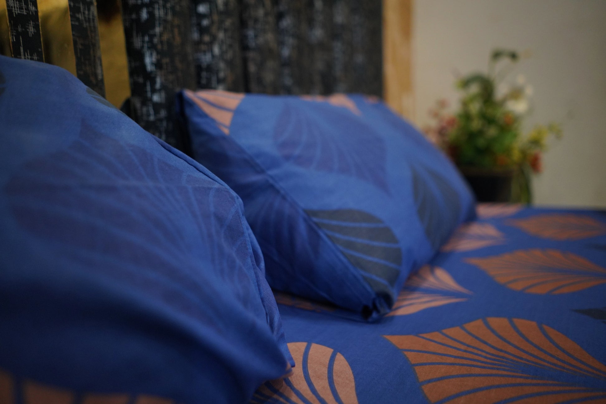 Blue pillows on a bed with a floral patterned headboard and blurred background