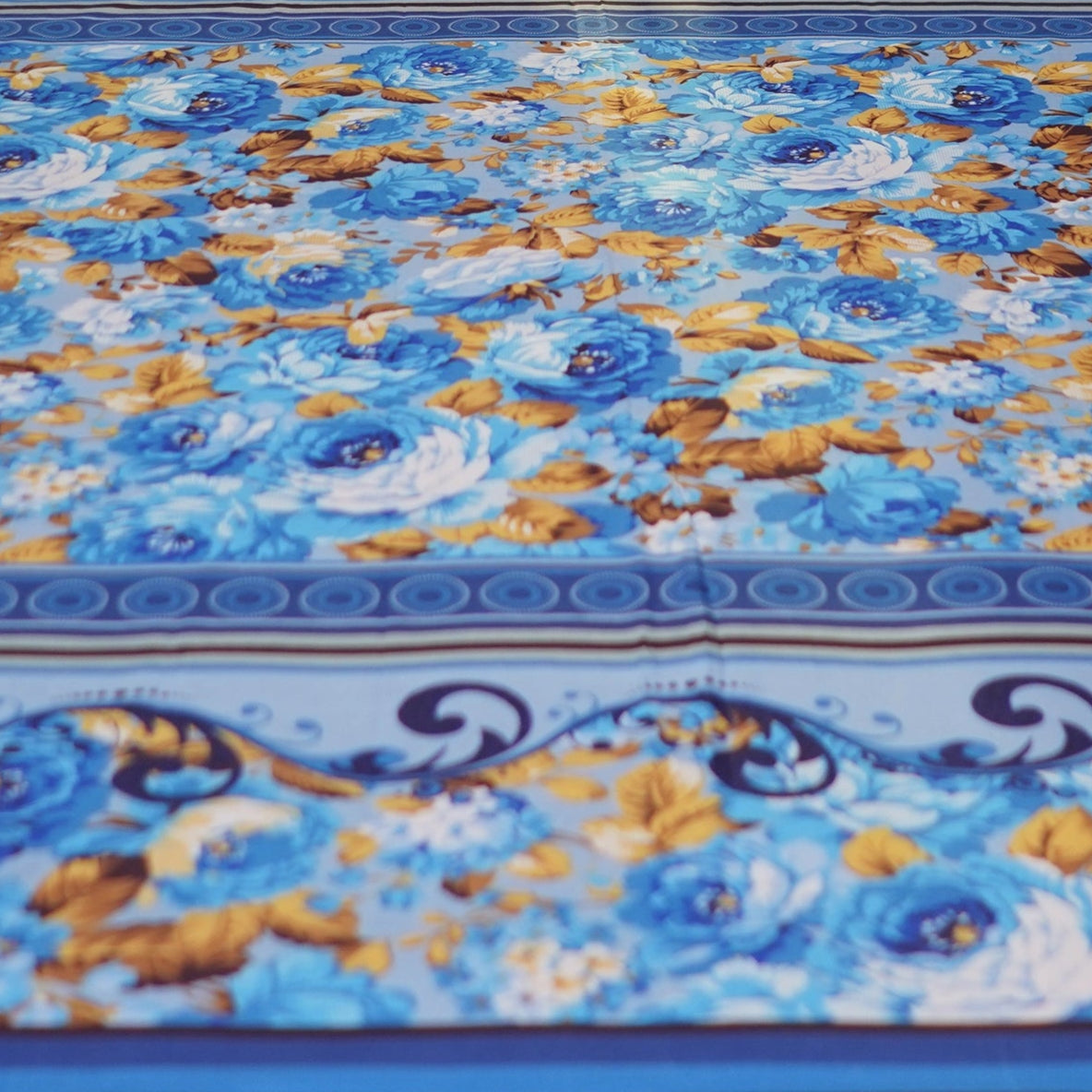 Bed with blue floral bedding and decorative pillows against a patterned wall.