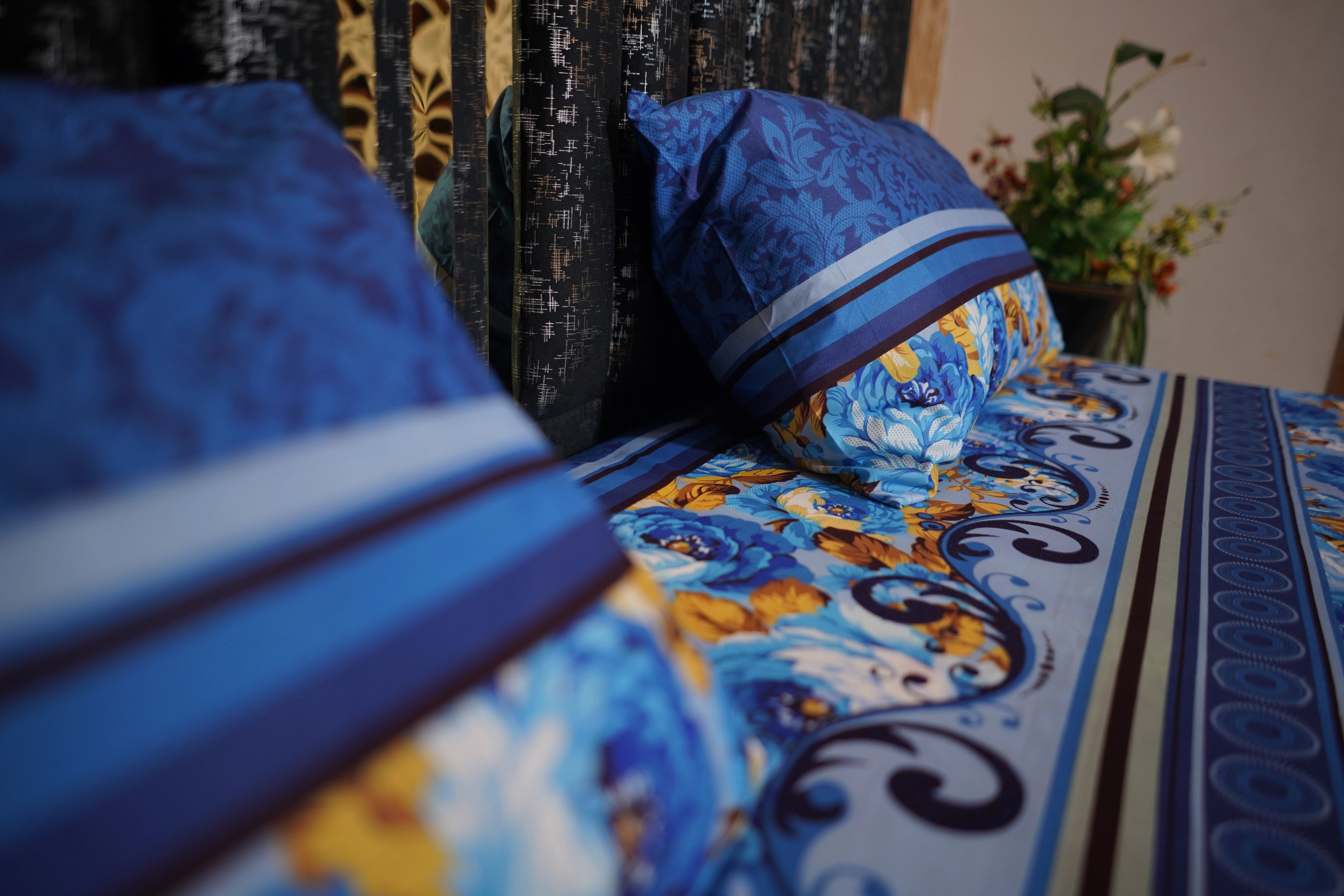 Decorative pillows with blue and yellow patterns on a bed with floral curtains.