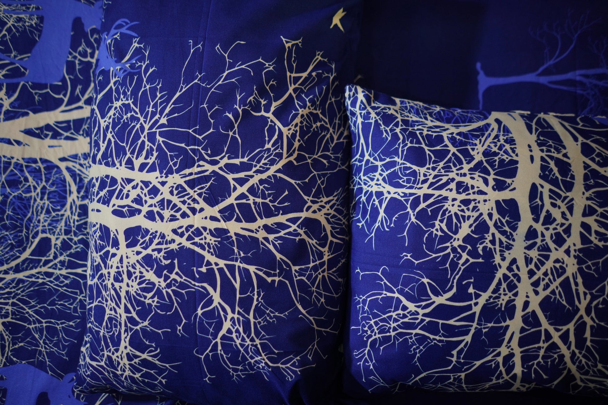 Two pillows with white tree branch patterns on a blue background