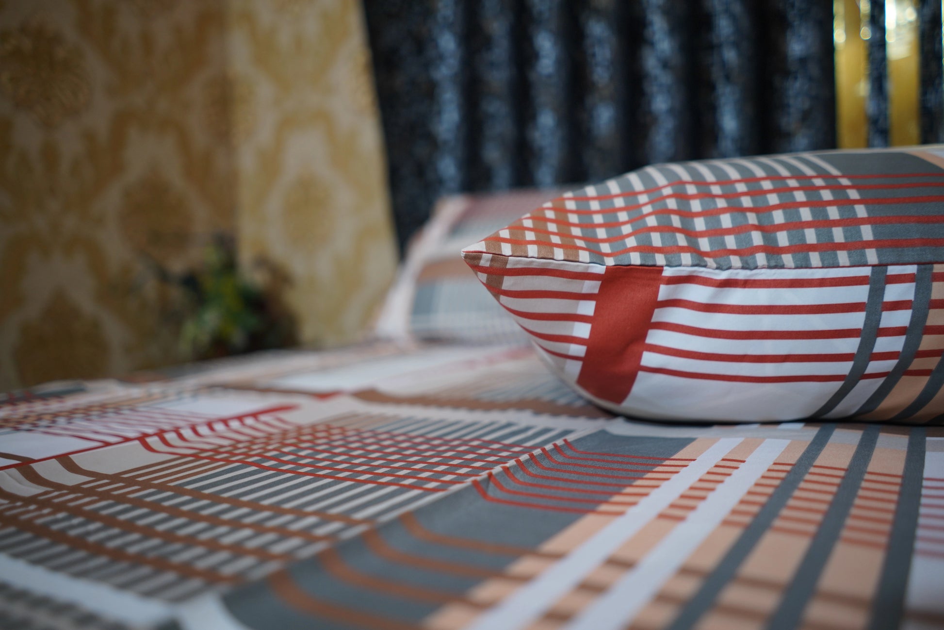 Striped pillow on a bed with a patterned bedspread and blurred background