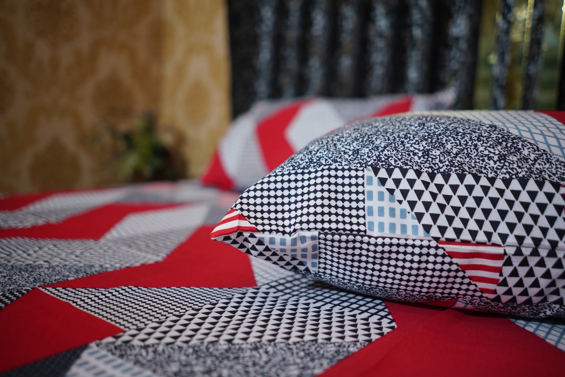 Patterned pillow on a red and gray quilt with blurred background