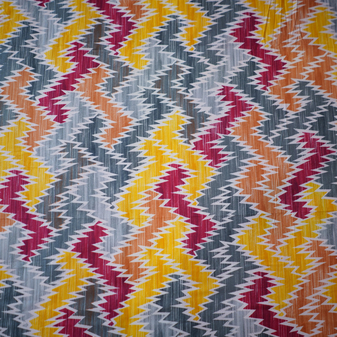 Bed with colorful zigzag pattern bedding set in a room with large windows.