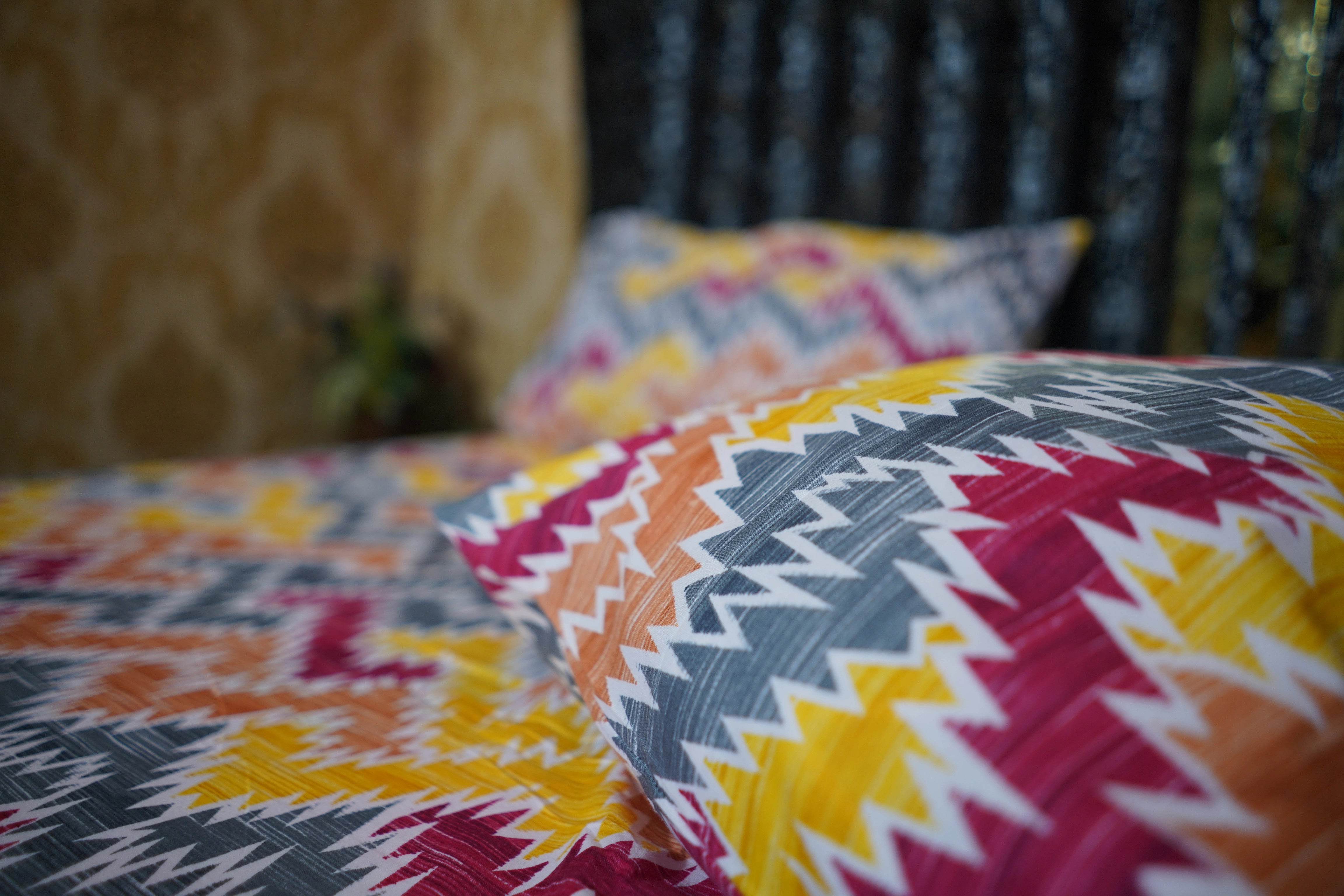 Colorful geometric-patterned pillows on a bed with a blurred background