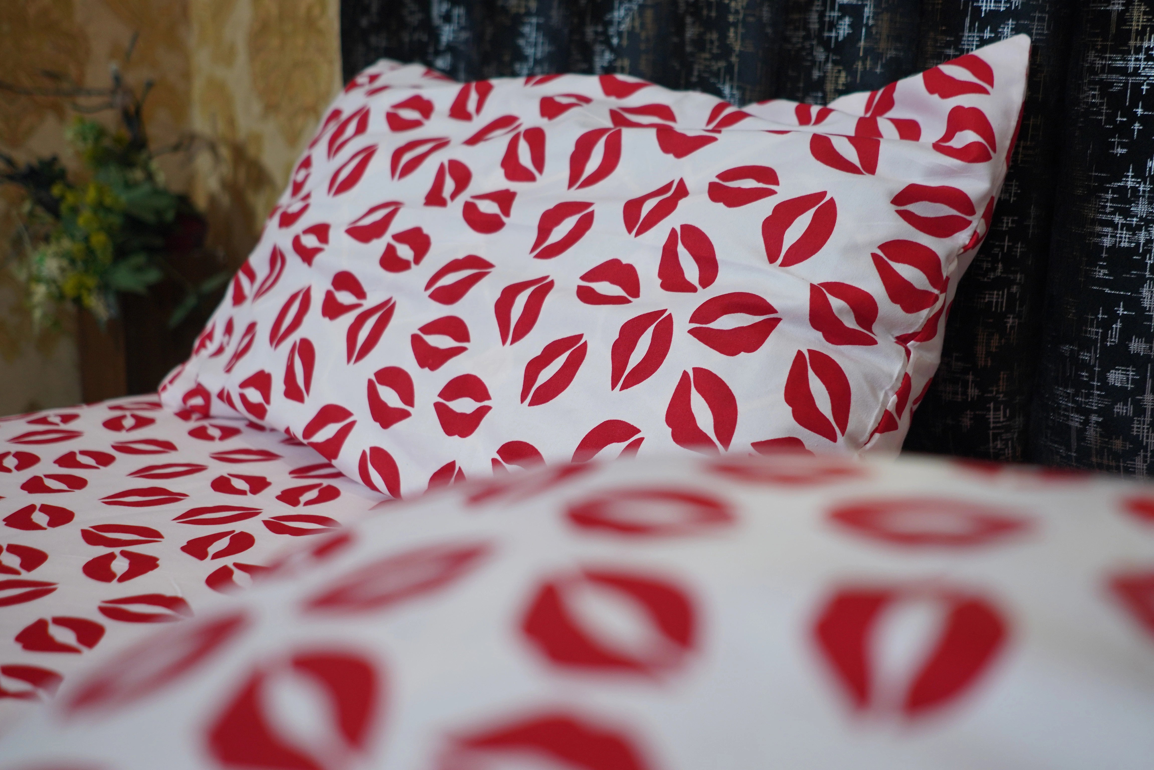 Red lip print pattern on white fabric with a pillow in the background
