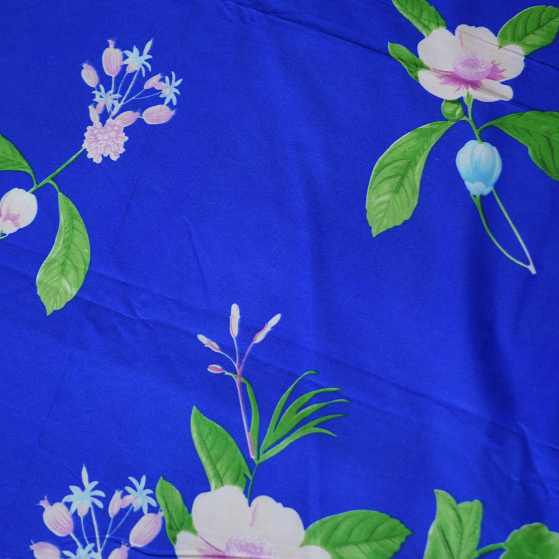 Blue floral bedding set on a bed in a bright room with curtains and a lamp.
