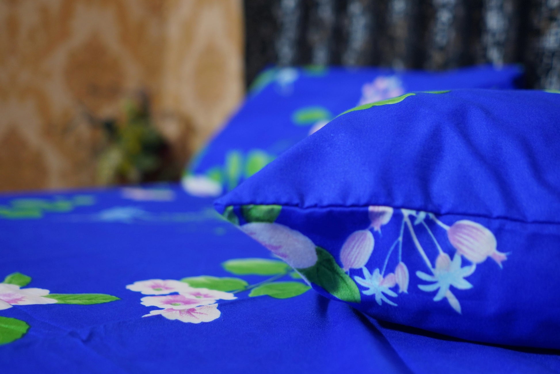 Blue floral-patterned bedspread and pillows on a bed with a blurred background