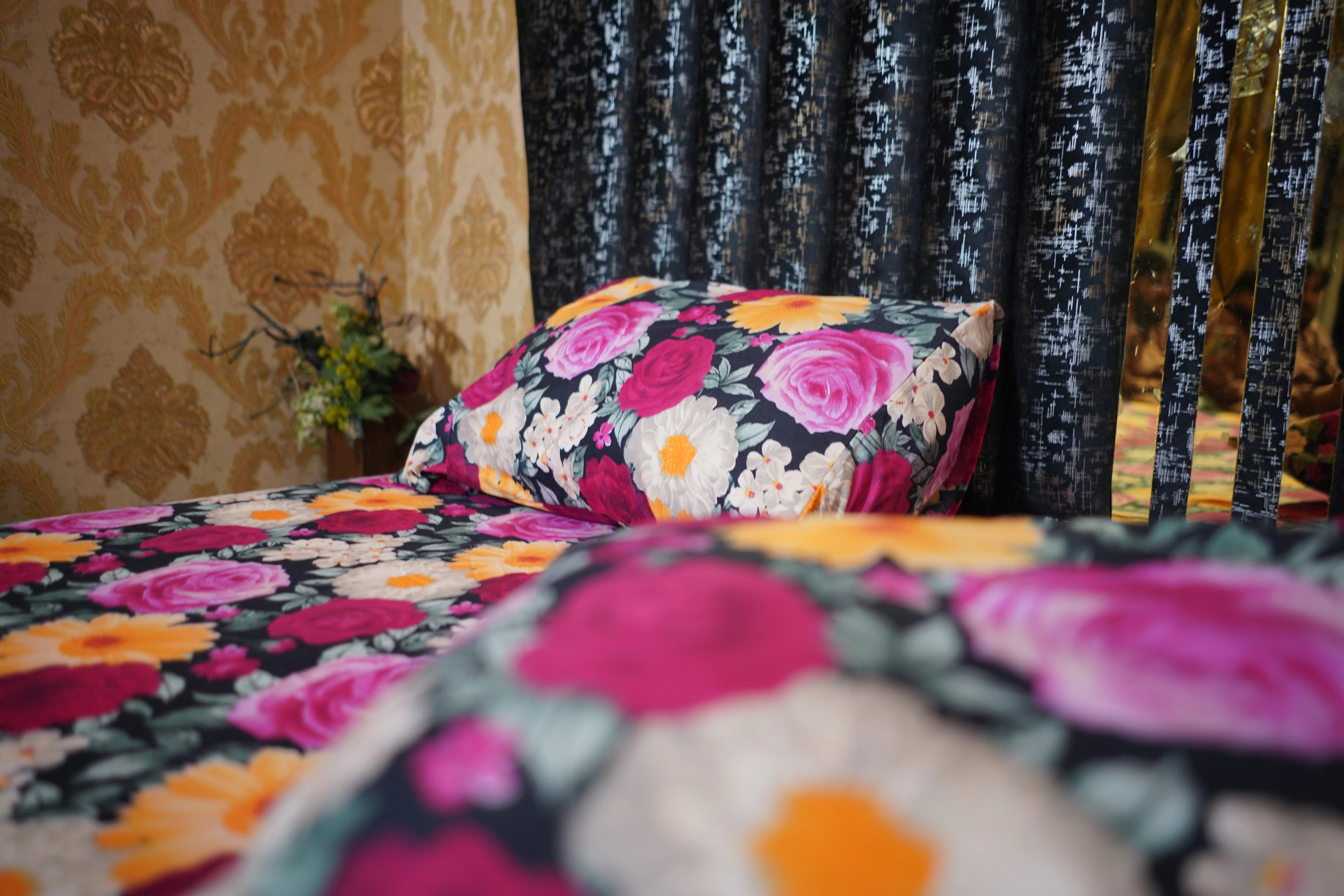 Floral-patterned bedspread and pillows on a bed with decorative curtains.