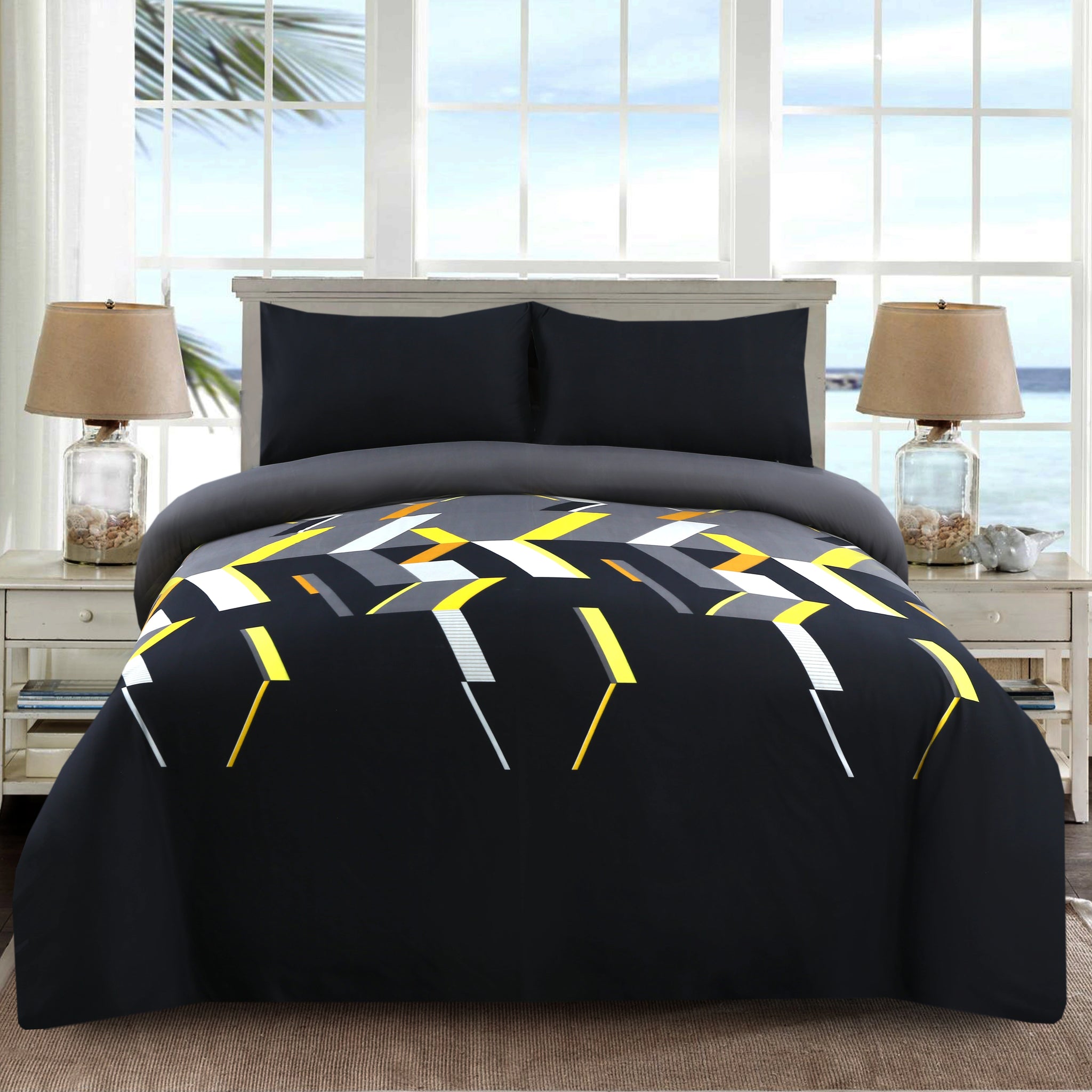Bed with geometric patterned comforter in a room with large windows.