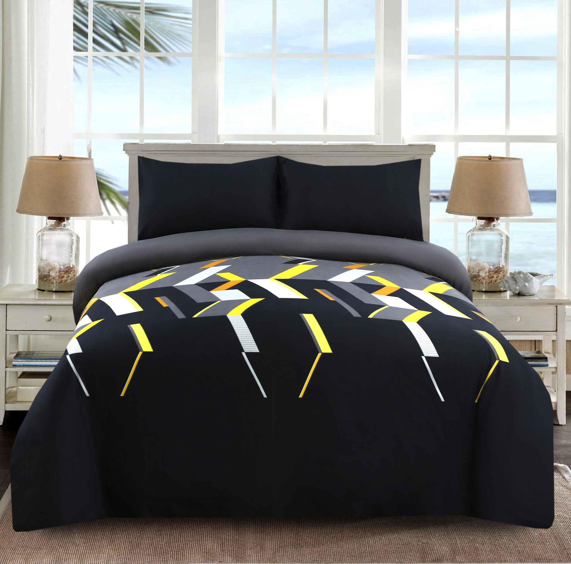 Bed with geometric patterned comforter in a room with large windows.