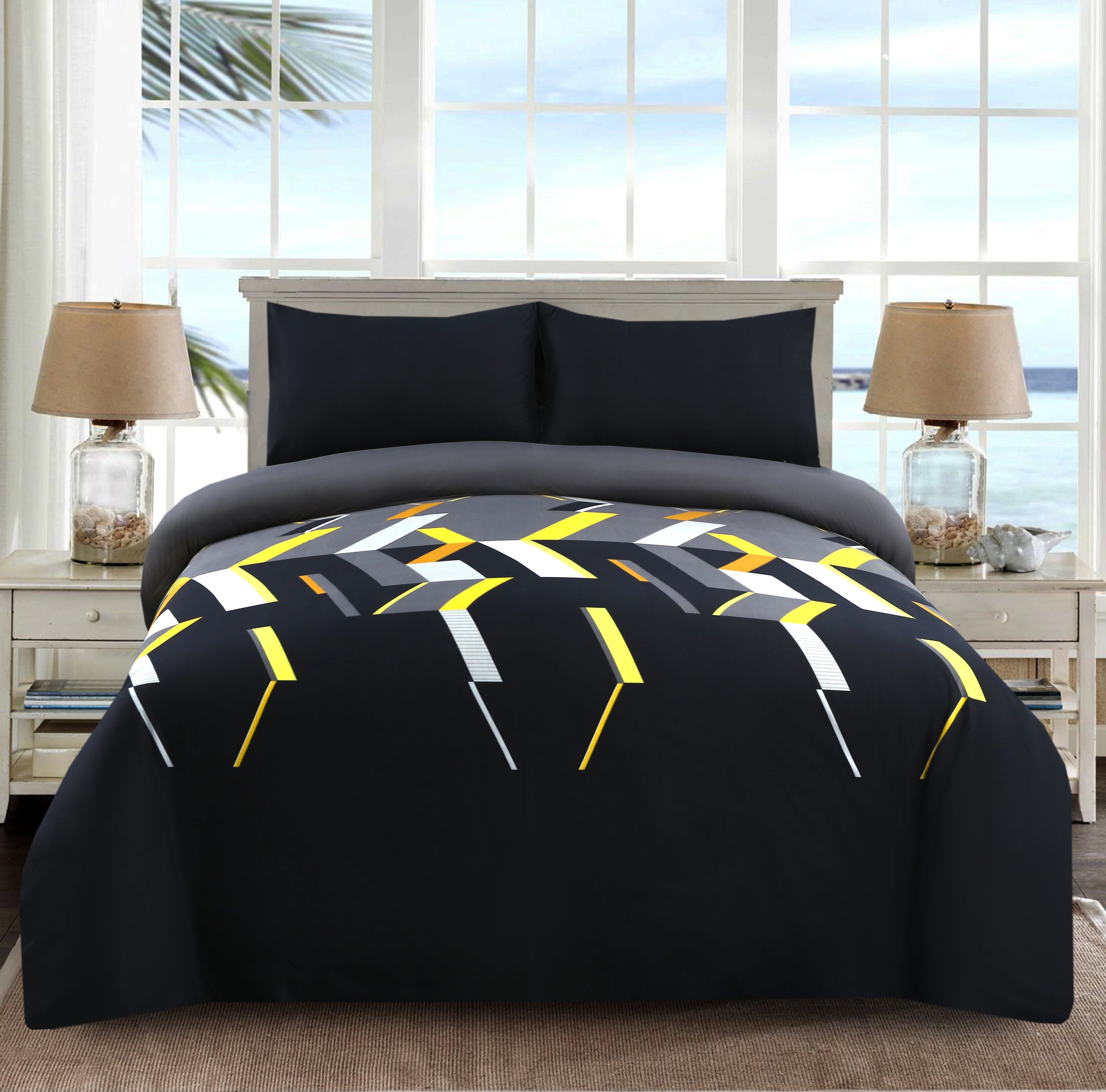 Bed with geometric patterned comforter in a room with large windows.