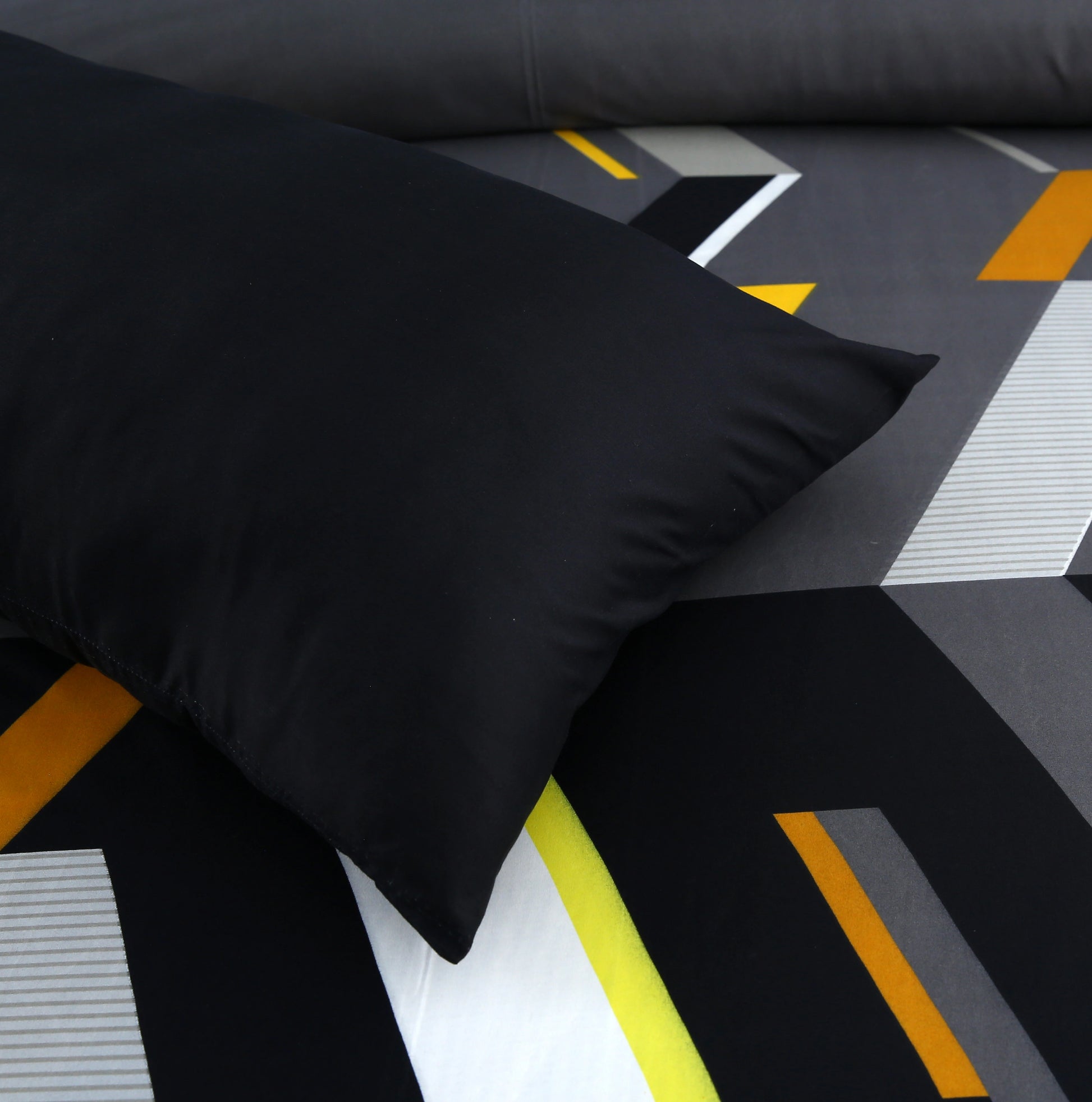 Black pillow on a geometric-patterned bedspread with orange and gray lines.
