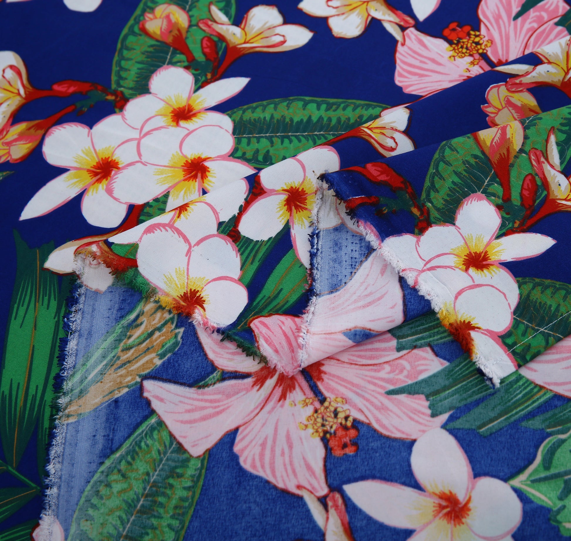 Close-up of tropical floral fabric with pink, white, and green flowers on a blue background.
