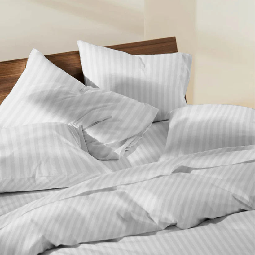 White striped bedding set on a bed with a wooden headboard.