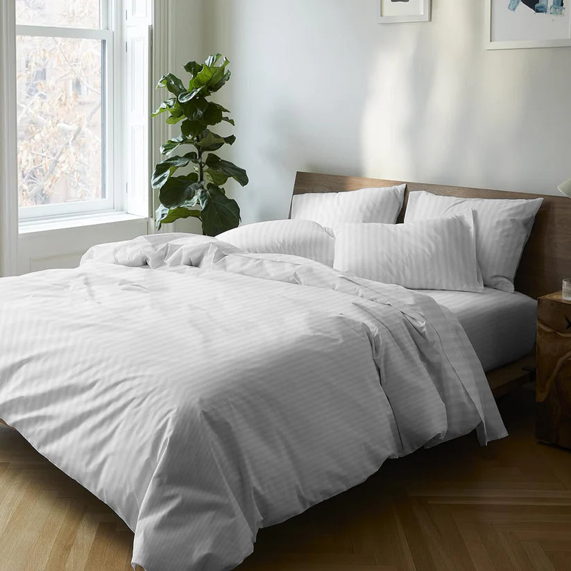 Neatly made bed with white bedding in a bright bedroom with a plant and window.
