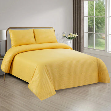 Yellow bedding set on a bed in a bright bedroom with a window and lamp.