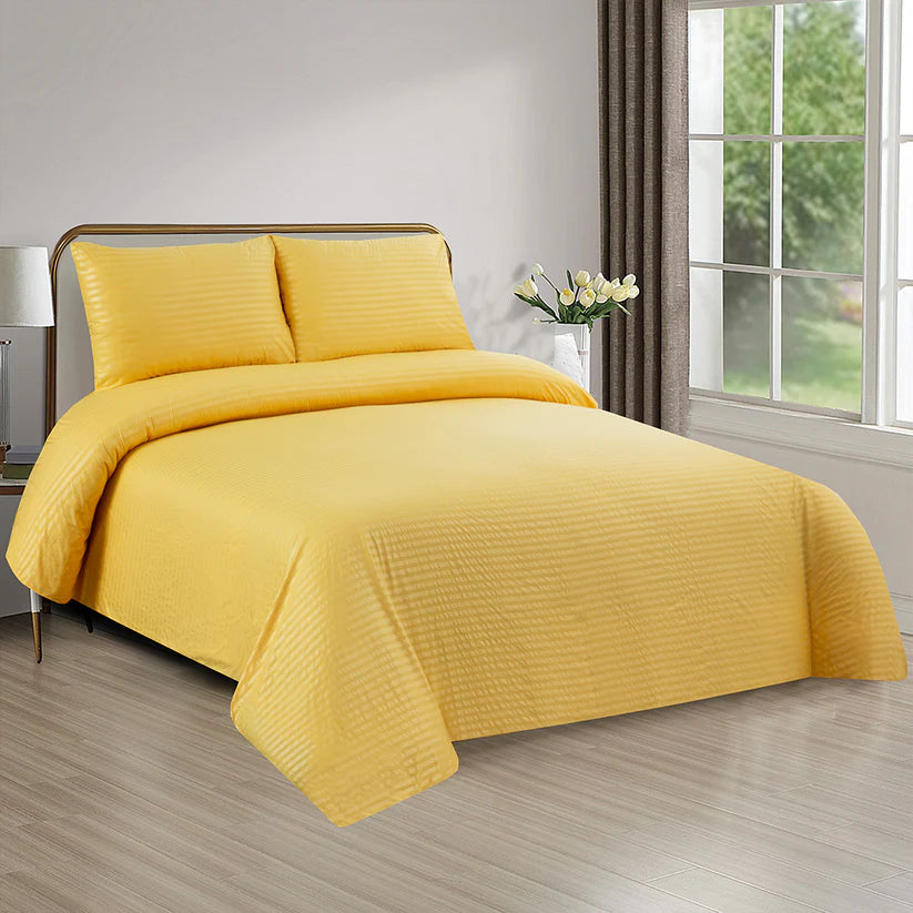 Yellow bedding set on a bed in a bright bedroom with a window and lamp.