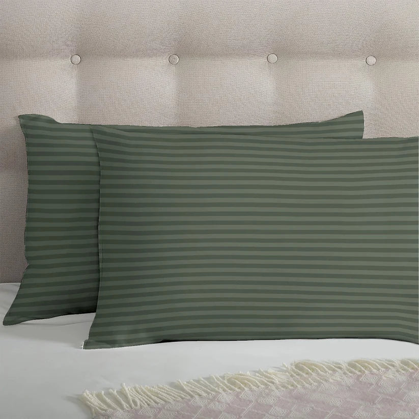 Green striped bedspread set on a bed in a bedroom with a plant and framed pictures.