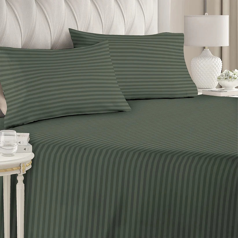Green striped bed sheets on a bed with a lamp and side table in the background.